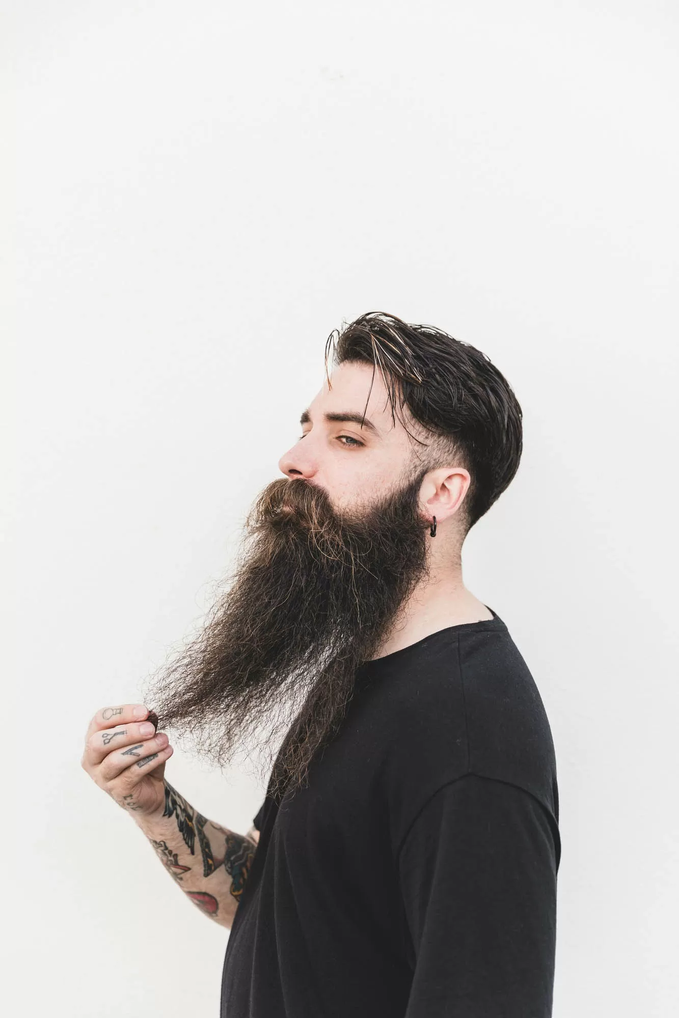 confident man touching his beard standing against white backdrop